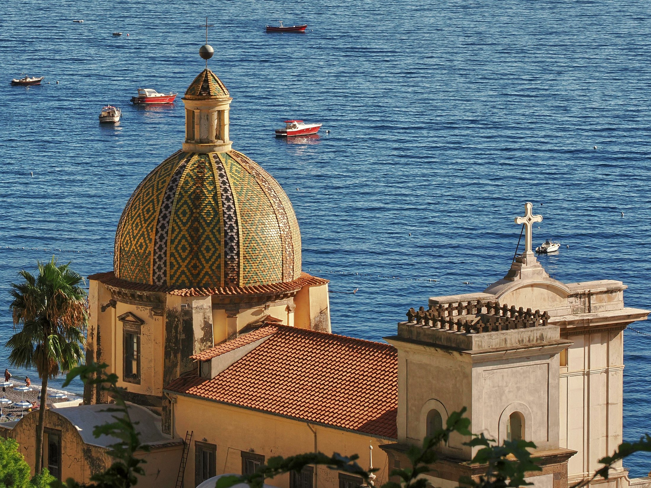 Cúpula de mosaico e iglesia frente al mar Mediterráneo, con barcas ancladas en la bahía